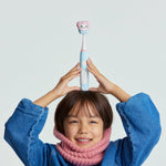 Child holding a pastel blue Ordo Sonic Kids rechargeable toothbrush topped with a Squishmallows Zozo character cap above their head.
