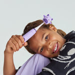 Child holding a purple Ordo Sonic Kids toothbrush topped with a bat-themed Squishmallows squish cap and smiling