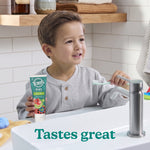Young child at a bathroom sink holding a Tom’s of Maine toothpaste tube and a toothbrush, text reads Tastes great