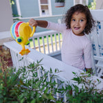 Smiling child on a porch holding and pouring a yellow striped bug watering can over plants