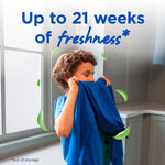 Child smelling a blue shirt in a laundry room with text ‘Up to 21 weeks of freshness’ and floating green leaves