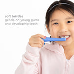 Child holding a blue toddler toothbrush to teeth with caption describing soft bristles for young gums.