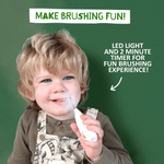 Young child smiling while holding a Jack N' Jill Tickle Tooth electric toothbrush with on-image text about LED light and two-minute timer