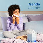Child on a bed holding a tissue with a Puffs Ultra Soft cube placed on the blanket beside plush toy