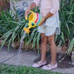 Child standing outdoors watering plants with a yellow striped bug-shaped can that sprays water from a flower spout