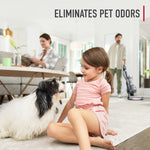 Lifestyle image of a child sitting on a carpet facing a dog with a person vacuuming in the background