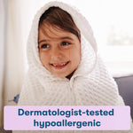 Close-up lifestyle image of a smiling child wrapped in a white towel with a dermatologist-tested claim panel