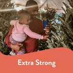 Person holding a blue patterned Chinet cup while carrying a child among Christmas trees, with "Extra Strong" text.