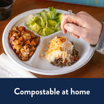 Hand using a fork to eat from a Chinet three-compartment white paper plate filled with salad, roasted vegetables and shepherd's pie.