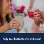 Two hands clinking Chinet Crystal clear plastic cups filled with light colored beverages at a gathering