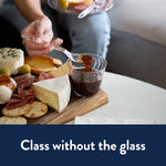 Person using a clear plastic spoon to serve a fig jam from a small cup on a charcuterie board in a lifestyle setting