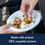 Hand holding a Chinet white paper bowl of popcorn and pretzels, fingers reaching into the snack in a casual setting