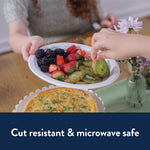 Person handing a white Chinet oval platter filled with sliced kiwi, strawberries and blackberries at a table