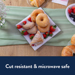 Top-down view of a Chinet square plate arranged with donuts, pastries and strawberries on a wood table with a green runner.