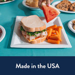 Chinet square plate with a sandwich and baby carrots, surrounded by other plates and a hand reaching for a slice of watermelon.