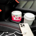 Citrus Magic Dragonfruit solid air freshener sitting in a car cupholder beside a coffee cup and phone
