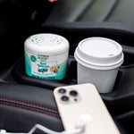 Citrus Magic Auto Sea Breeze air freshener tub sitting in a car cup holder next to a coffee cup and phone