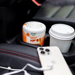 Citrus Magic Tropical Citrus air freshener placed in a car cupholder beside a takeaway coffee cup and smartphone.
