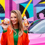 Smiling model holding a Citrus Magic Tropical Citrus air freshener and a matching spray bottle in front of a colorful mural.
