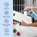 Hand holding a CleanBoss spray bottle, spraying a white cutting board on a kitchen countertop with icons at left