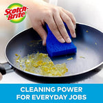 Hand using a blue Scotch-Brite non-scratch sponge to clean residue from a nonstick frying pan