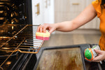 Person using a Scrub Daddy sponge to clean an oven rack while holding a Scrub Daddy Cif cleaning bottle