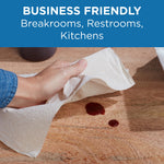 Hand using a Pacific Blue Select paper towel to clean a spill on a wooden surface, with business-friendly label above.