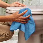 Person using a blue microfiber cloth to clean the exterior of a toilet in a bathroom setting.