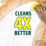 Hand holding a yellow sponge cleaning a surface with large text reading CLEANS 4X BETTER on a foam background