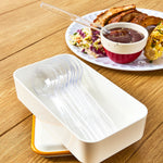 Clear disposable jumbo spoons displayed in a white tray with a plate of food and a spoon in sauce in the background