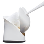 White toilet brush being lifted from a curved white hideaway holder, showing the brush shield and holder opening