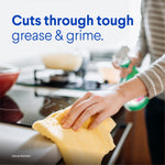 Person wiping stovetop with cloth while holding a Clorox Clean-Up spray bottle; text reads "Cuts through tough grease & grime"