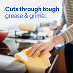 Lifestyle close-up of a person wiping a stovetop with a yellow cloth while holding a Clorox Clean-Up spray bottle in background.