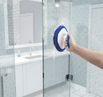 Person using Clorox diamond-shaped scrubber on glass shower door with bathroom vanity reflected in background