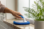 Hand holding Clorox diamond scrubber on a windowsill or countertop, showing textured blue pad and handle