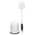 Full view of a white toilet brush with black-grip handle standing beside its white hideaway holder on a white background