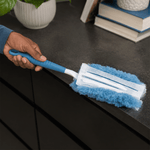 Close-up of a blue fluffy duster head being used to clean a dark countertop, showing the refill pad backing