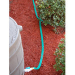 Close-up of a green garden hose running over red mulch between shrubs toward a barrel spigot
