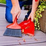 Close-up of hands using a red Libman whisk broom and dustpan to gather deck debris