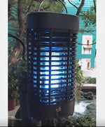 Close-up of a lit Black Flag bug zapper showing bright blue UV bulb inside protective black grille with outdoor background