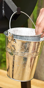 Close-up of a metal bucket with a Pit Boss foil bucket liner inside while a hand reaches into the liner, grill hardware visible above.