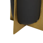 Close-up detail of a black planter seated in a textured gold metal stand, showing the stand's triangular foot and planter curve.