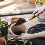 Close-up of a Fiskars trowel holding soil above a terracotta pot while a person steadies the pot