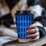 Close-up of hand holding a blue-patterned Chinet Comfort cup with a black lid against plaid fabric