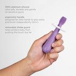 Close-up of a hand gripping a purple silicone toddler toothbrush with white guard and product text