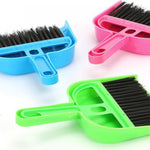 Close-up of three small plastic dustpans and brushes in blue, pink, and green showing brush bristles and molded handles on white.