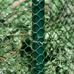 Close-up of hexagonal green plastic poultry netting fastened to a green metal stake in a grassy area
