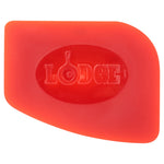 Close-up of a red Lodge silicone scraper showing the embossed Lodge logo centered in an oval on the tool.