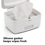 Close-up of a wipe emerging from inside an open white OXO dispenser showing silicone gasket