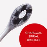 Macro view of a Colgate toothbrush head showing charcoal spiral bristles with a red circle label reading charcoal spiral bristles